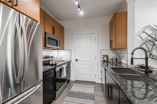 Galley kitchen with stainless refrigerator, range, and granite countertops with tile backsplash.