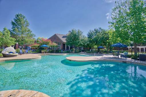 A large swimming pool surrounded by trees and umbrellas.