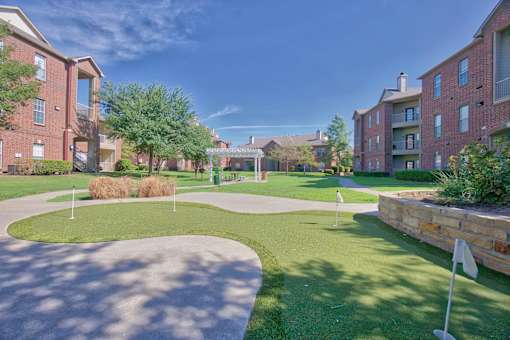 A sunny day at a residential complex with a green lawn and brick buildings.