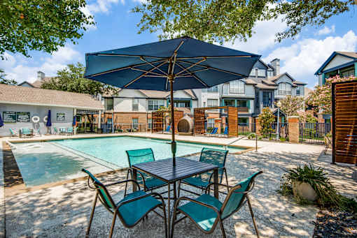 A poolside table with chairs and an umbrella over it.