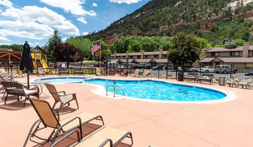 a pool with lounge chairs and a slide at the foot of a mountain