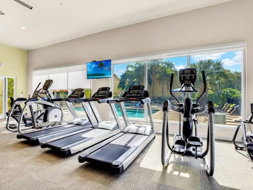 a gym with cardio equipment and a large window with a view of the pool