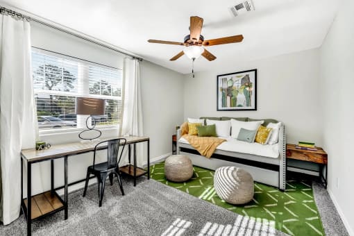 a living room with a ceiling fan and a couch with a desk in front of it