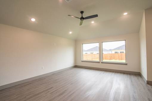 Empty room with a ceiling fan and two windows.