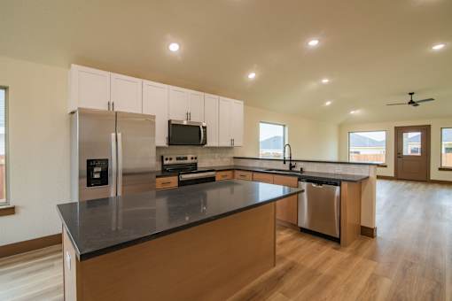 A kitchen with a black counter top and wooden floors.