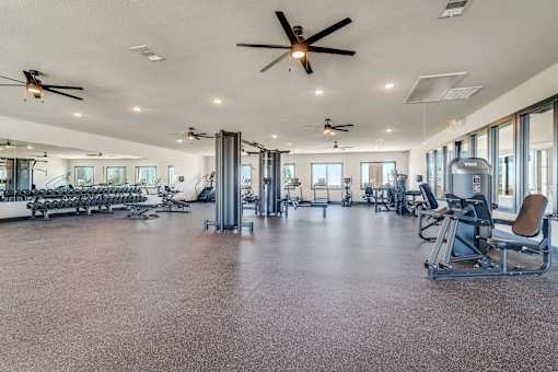 A spacious gym with a variety of equipment and a ceiling fan.