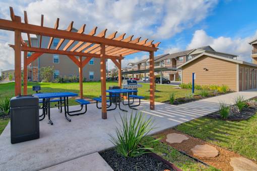 A wooden pergola with blue picnic tables underneath it.