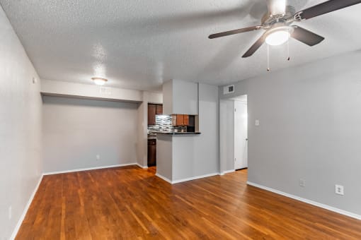 an empty living room with a ceiling fan and a kitchen