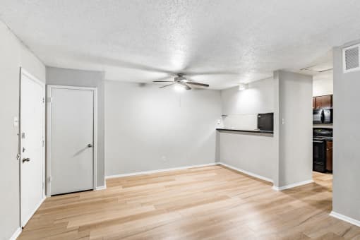 an empty living room with a ceiling fan and a kitchen
