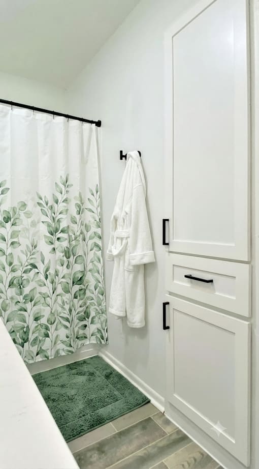A white bathroom with a green rug and a shower curtain with green leaves on it.