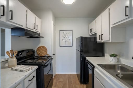 A black refrigerator sits in a kitchen with white cabinets.