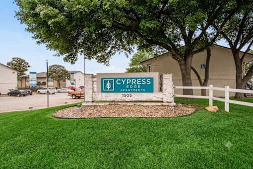 A sign for Cypress Apartment's 1505 is in front of a building.