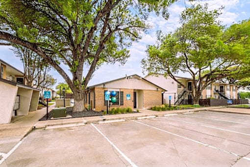 A parking lot in front of a building with a tree in the foreground.