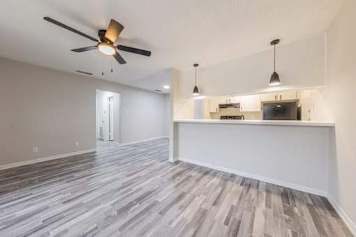 A room with a ceiling fan and a long wooden floor.