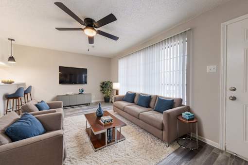 A living room with a brown couch, a white rug, and a ceiling fan.