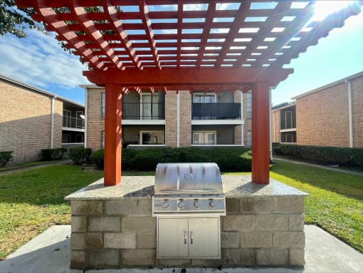 an outdoor kitchen with a grill and a pergola in front of an apartment building  at The Alara, Houston