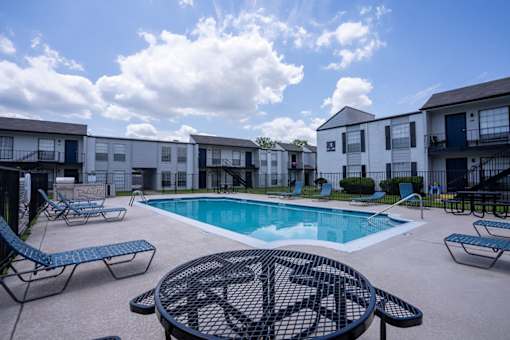A pool surrounded by chairs and a table in a courtyard.