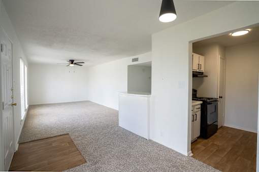 A room with a ceiling fan and a kitchen area in the back.