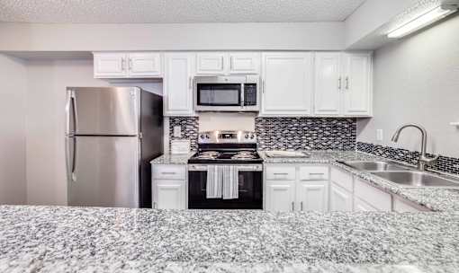 A kitchen with a refrigerator, microwave, oven, and sink.