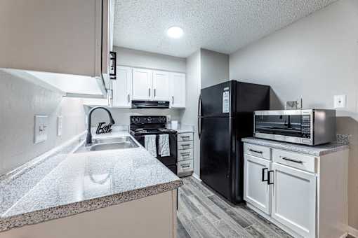 A kitchen with a black refrigerator and white cabinets.