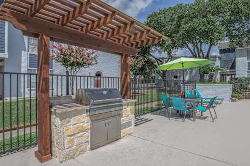 A wooden pergola with a grill and chairs under it.