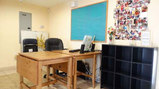 A room with a wooden desk and a bulletin board with pictures on it.