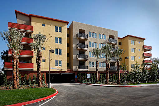 A large apartment complex with a red roof and palm trees in front.