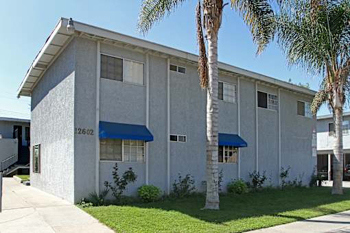 A building with a blue awning and palm trees in front.