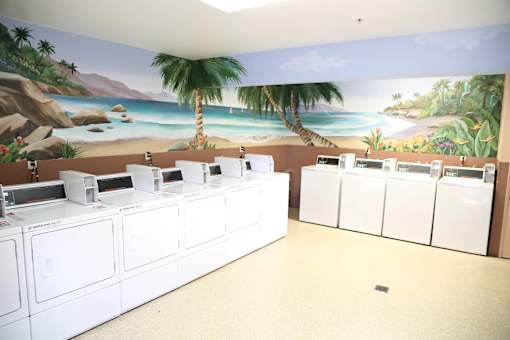 A row of washing machines in front of a painted beach scene.