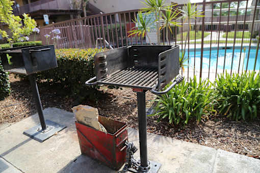 A barbecue grill is placed on a patio next to a pool.