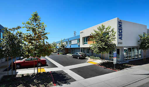 A red car is parked in front of a white building with the word "ASCENT" on it.