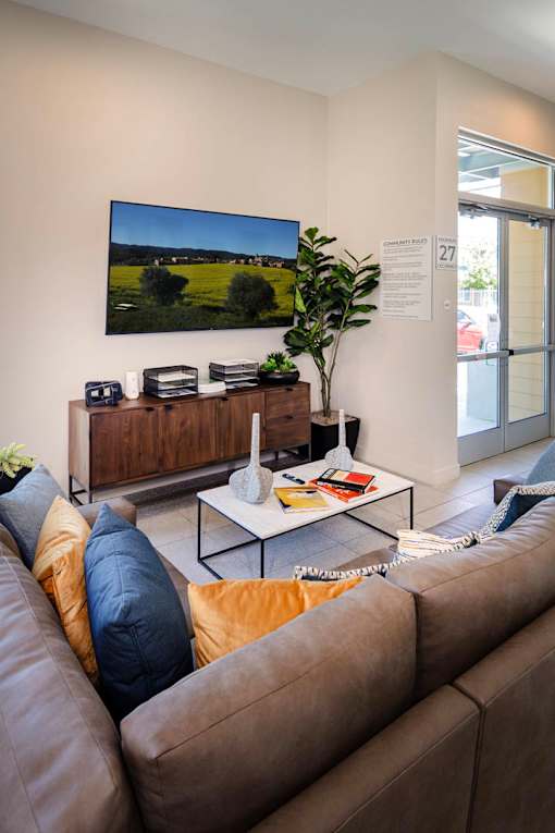 A living room with a brown couch and a flat screen TV mounted on the wall.