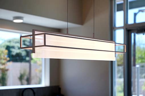 A modern light fixture hangs from the ceiling in a room with a view of the outdoors.