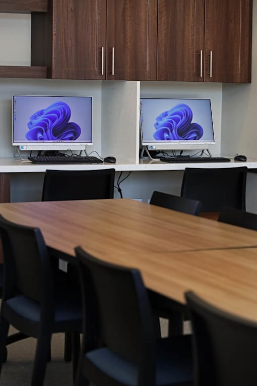 A conference room with a table and chairs and two monitors on the wall.