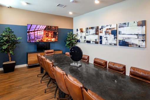 A conference room with a long table and chairs, a television, and a wall of paintings.