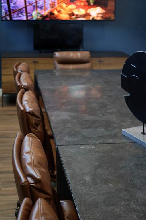 A row of brown leather chairs are lined up in front of a television.