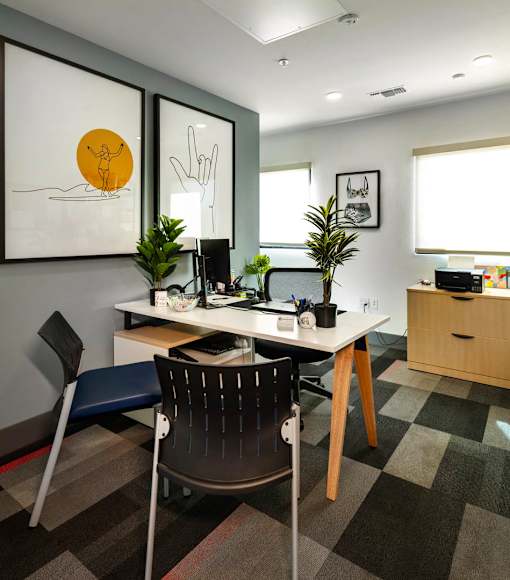 A room with a desk and chair in front of a wall with two framed pictures.