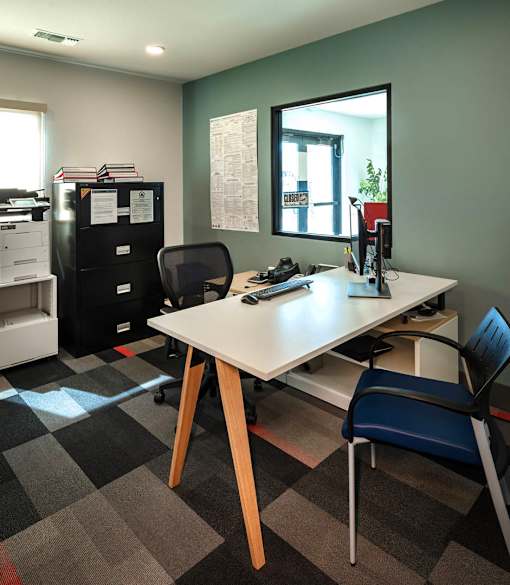 A black fridge sits next to a desk with a computer on it.