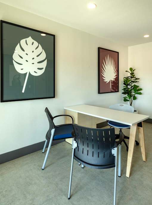A white table with a black chair and a leaf picture on the wall.