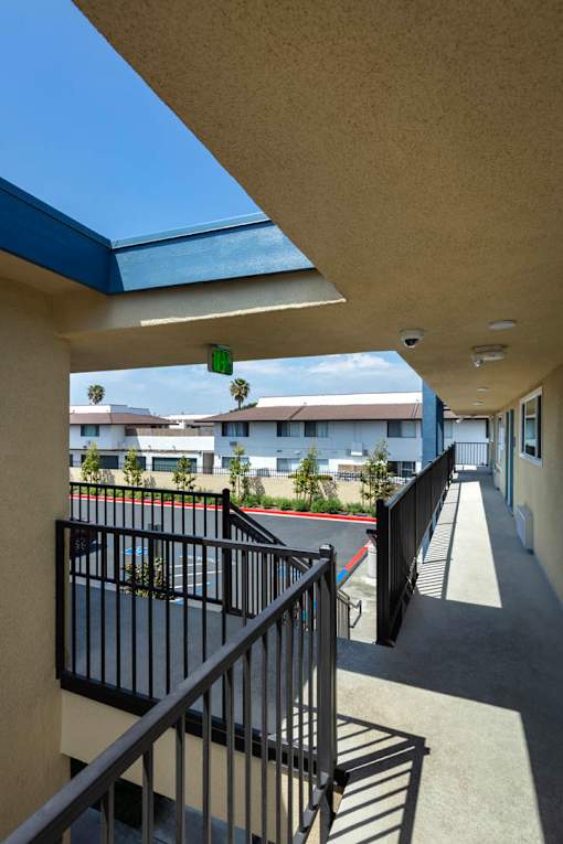 A balcony with a black railing and a view of a tennis court and buildings.