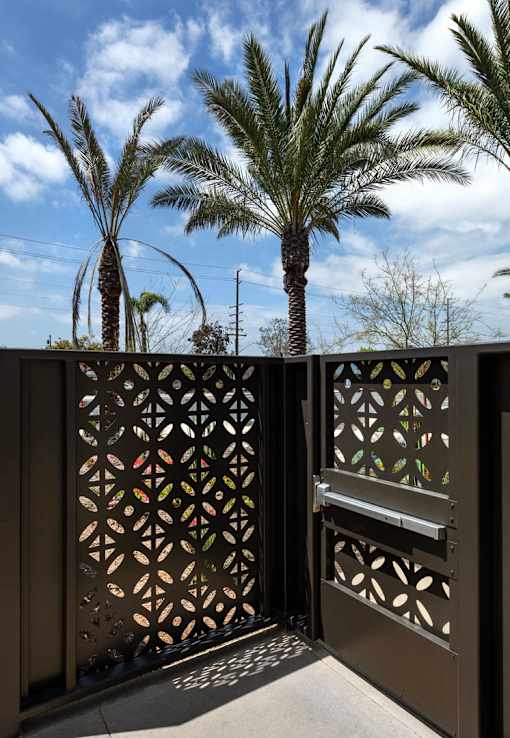 A gate with a decorative design is open to a patio with a palm tree.