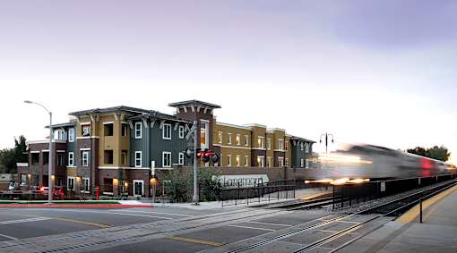 A train is coming down the tracks in front of a building.
