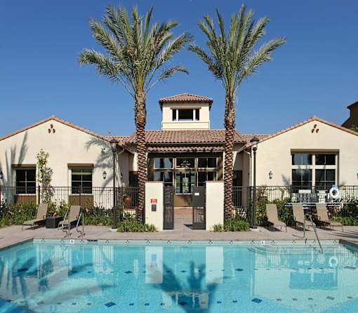 A pool in front of a house with palm trees.