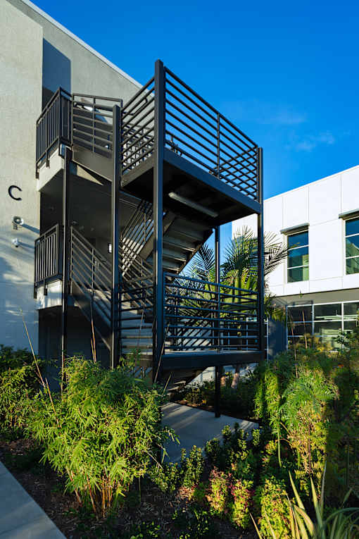 A modern staircase with metal railings is surrounded by green plants.