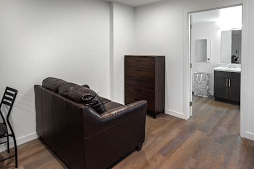 A brown couch with a blanket on it sits in a room with a wooden dresser and a mirror.