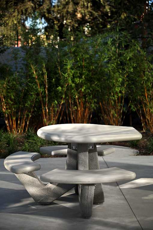 A grey table and two chairs are in front of a green shrubbery.