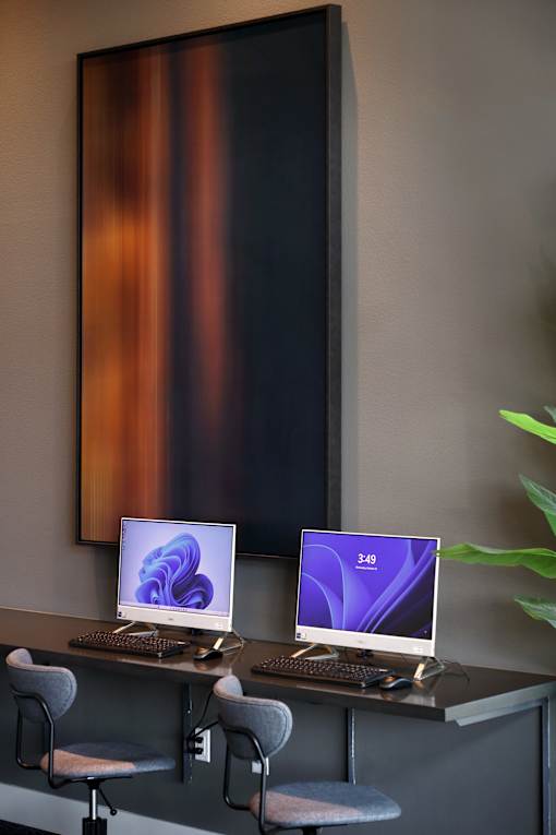 Two computers are on a desk with chairs.