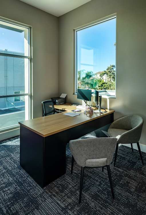 A room with a desk and chairs with a window in the background.