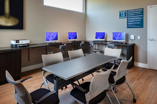 A room with a long table and chairs with computers on the table.