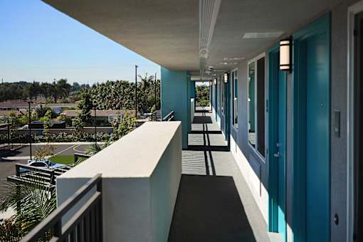 A long hallway with blue doors and a balcony overlooking a residential area.